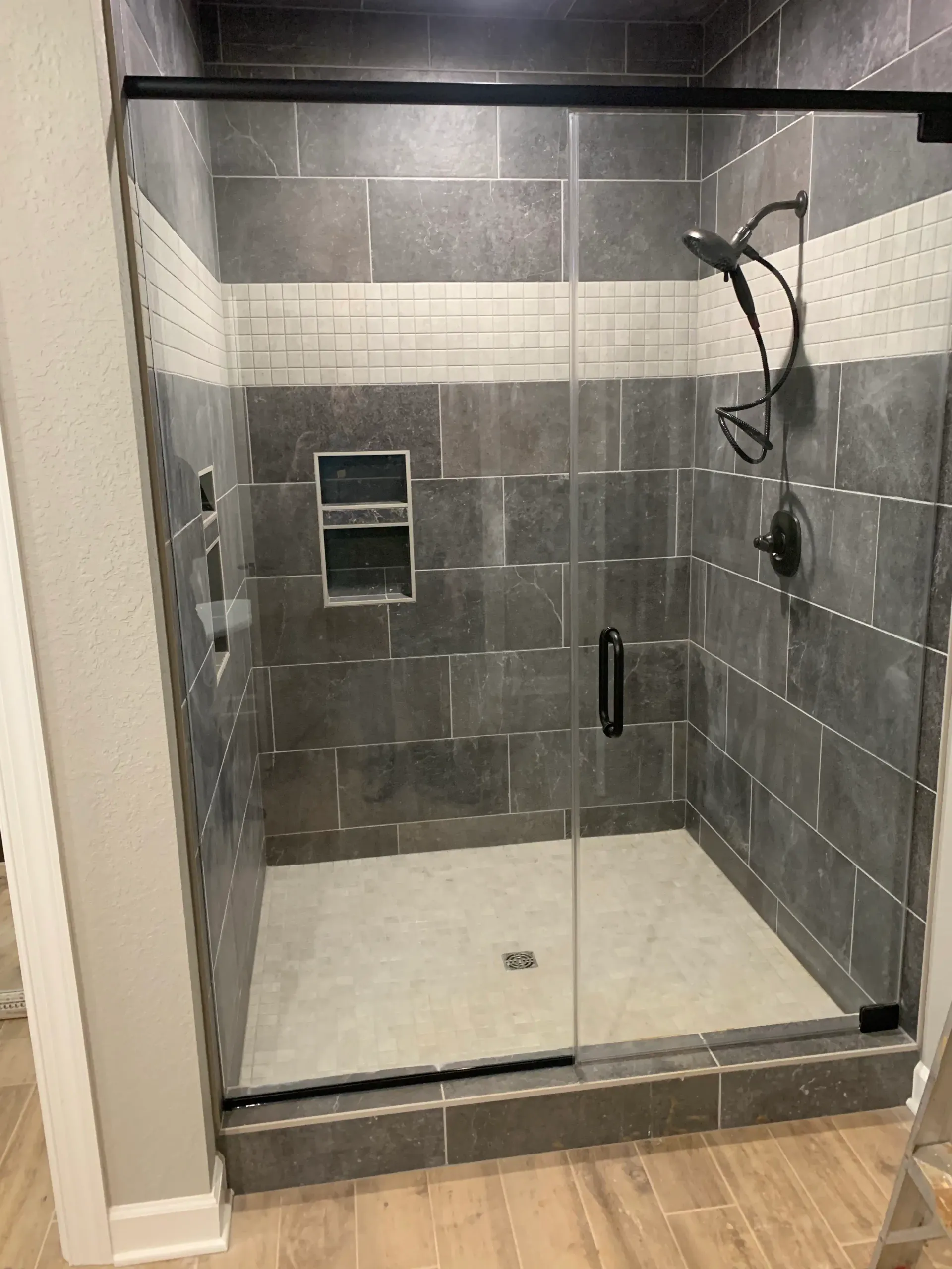 Gray tile shower with white accent band, glass door, and recessed niche