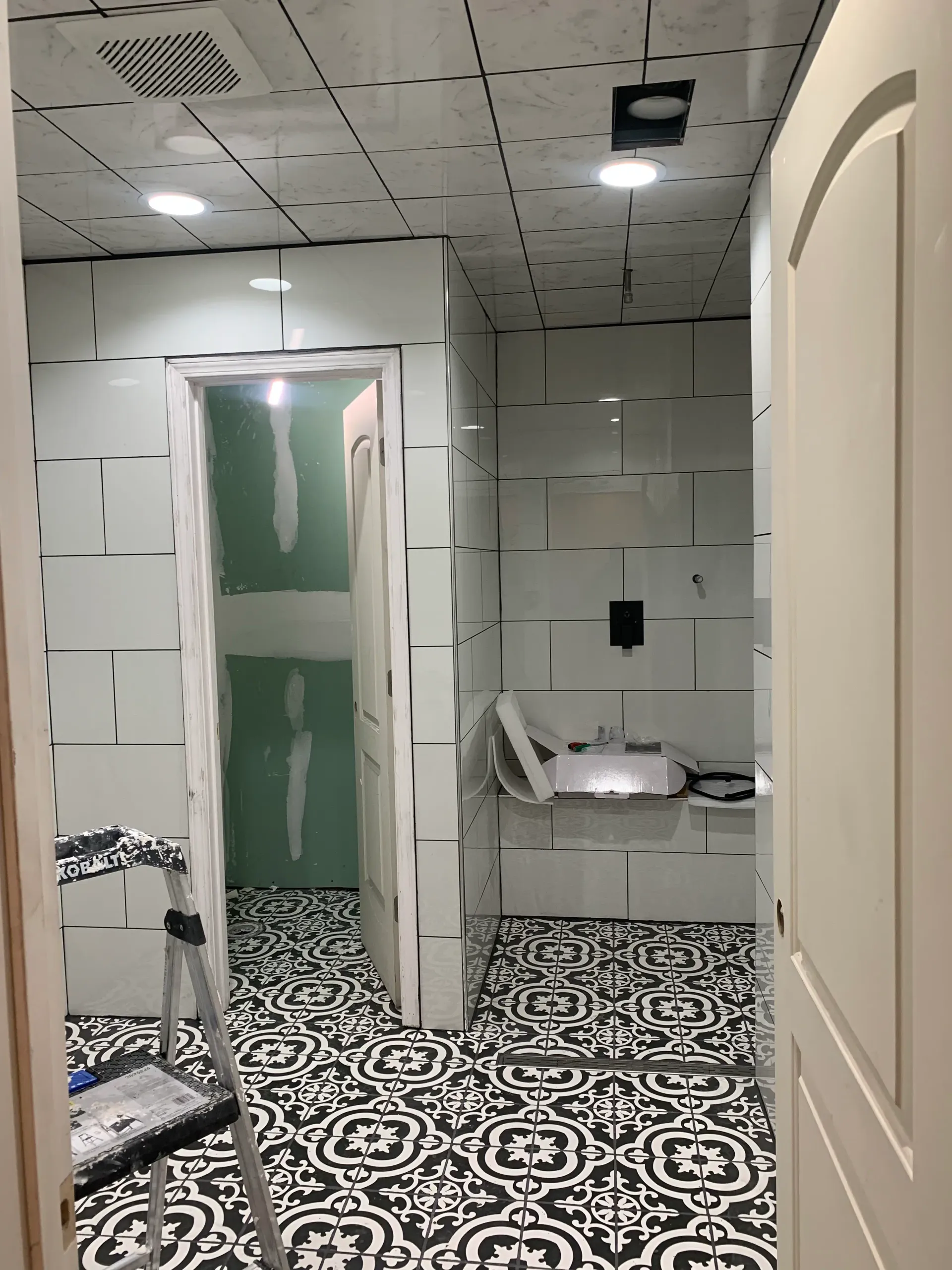 Bathroom remodel in progress with patterned tile floor, tiled walls, and stepladder
