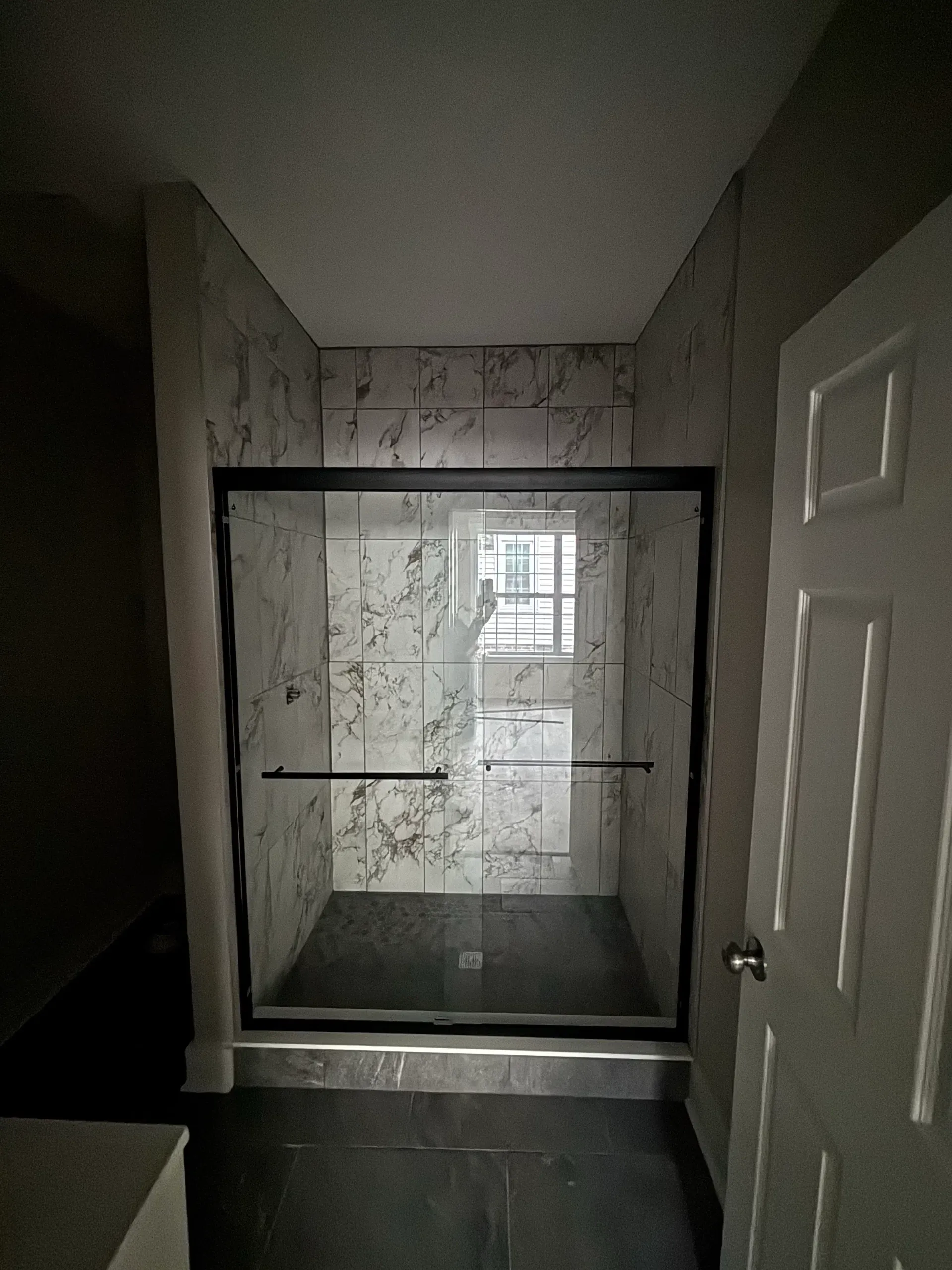 Marble-look tiled shower with black-framed glass door