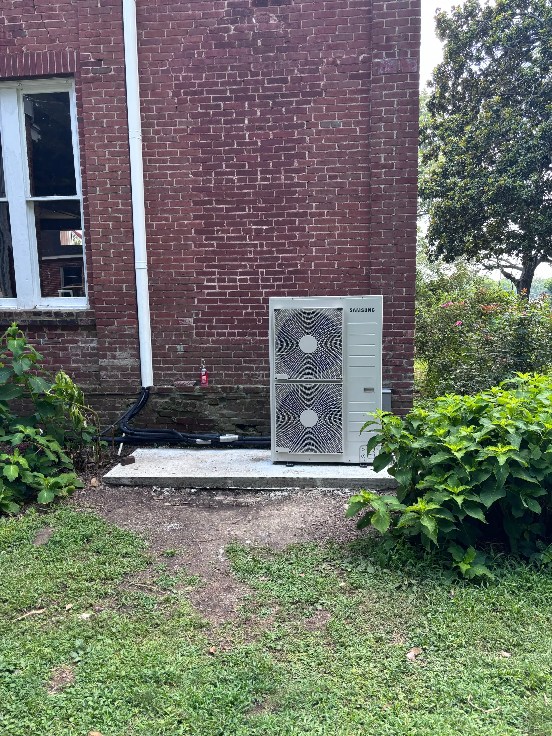 Samsung VRF outdoor unit installed on a concrete pad beside a brick building
