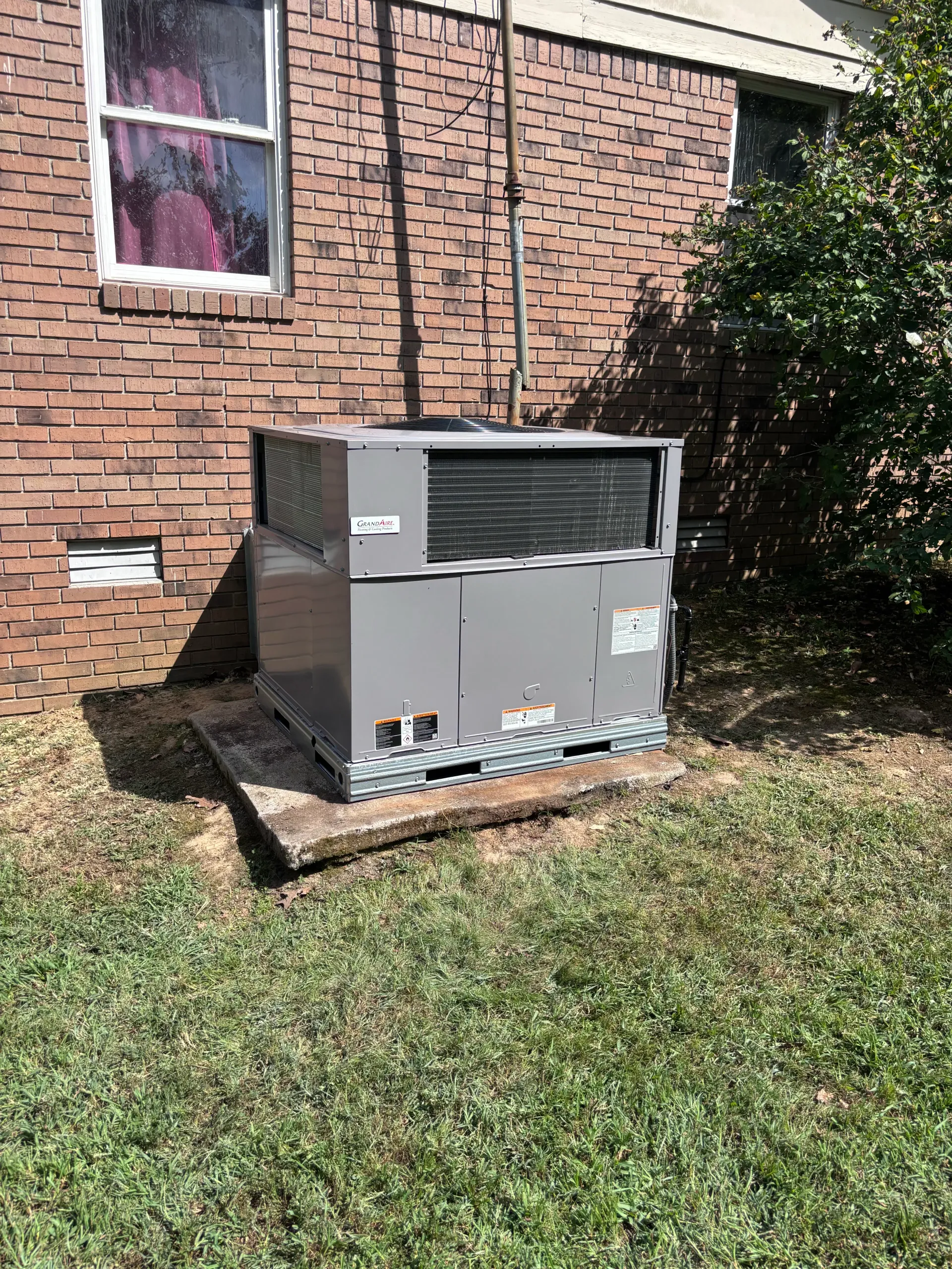 New outdoor package HVAC unit set on a concrete pad beside a brick home