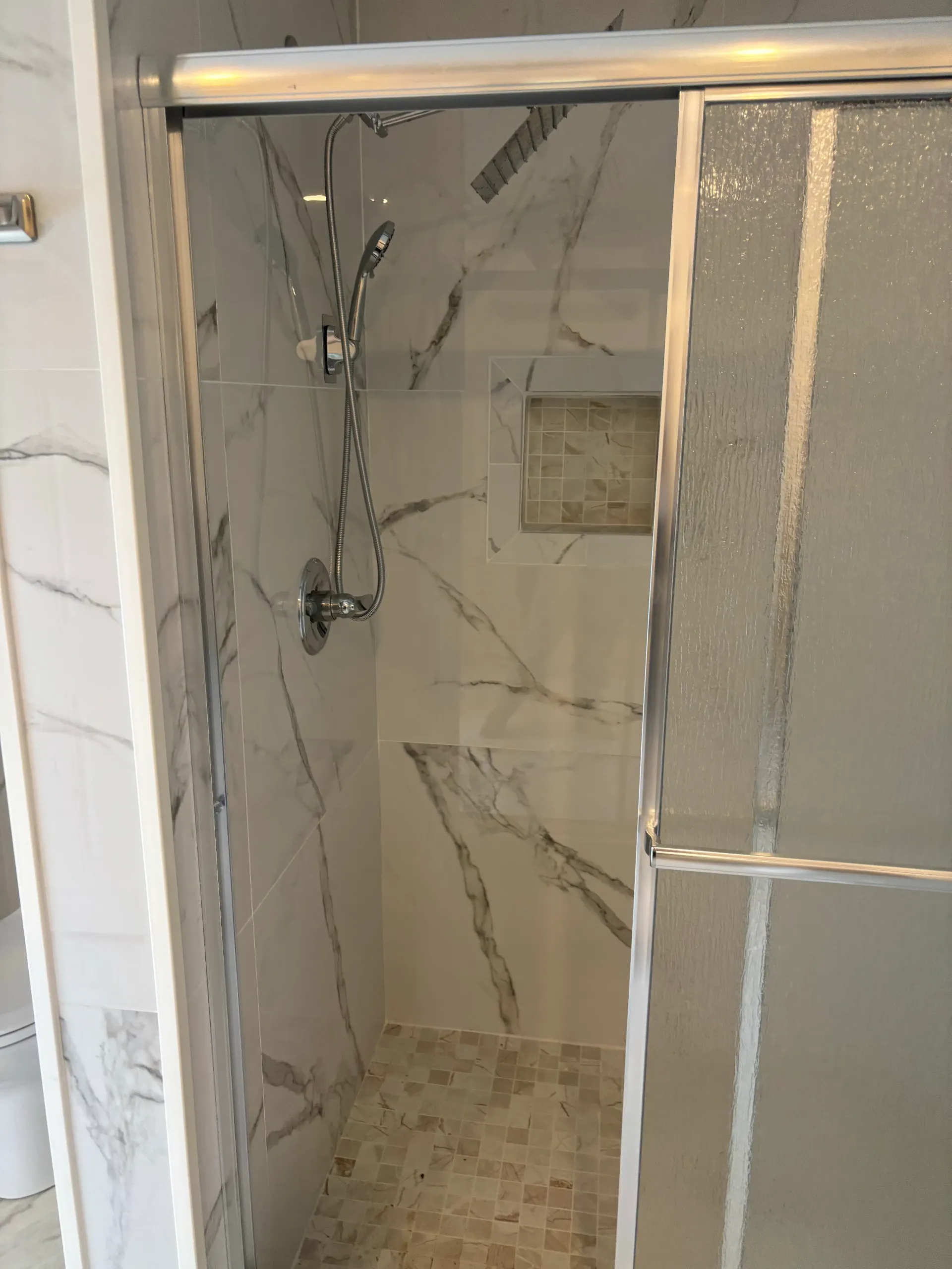 Marble tile shower with sliding glass door and handheld shower